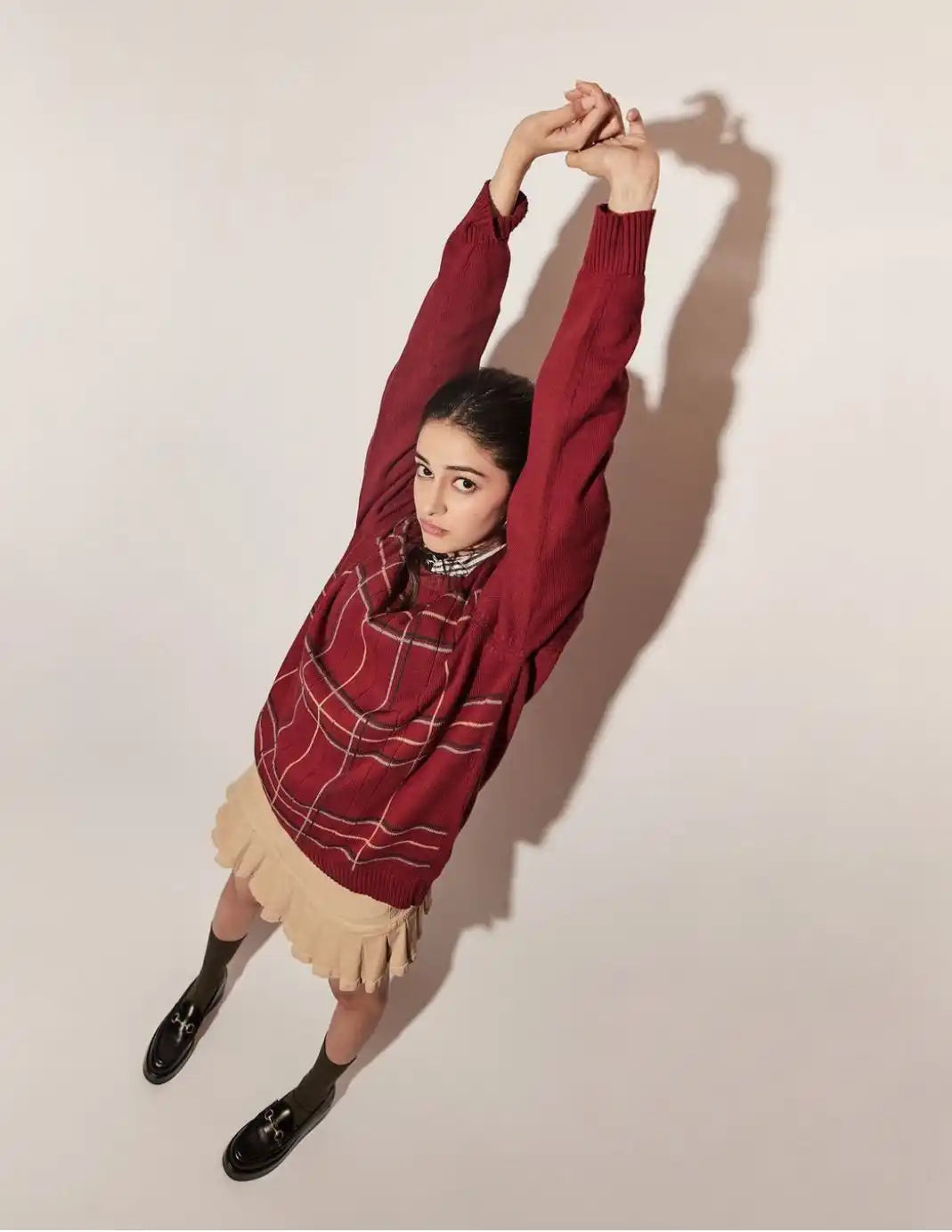 Person wearing a burgundy plaid shirt stretching their arms upward.