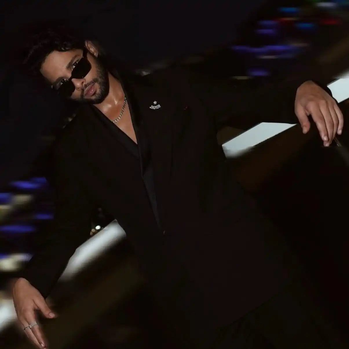 A person wearing sunglasses and a black outfit in a dark setting.